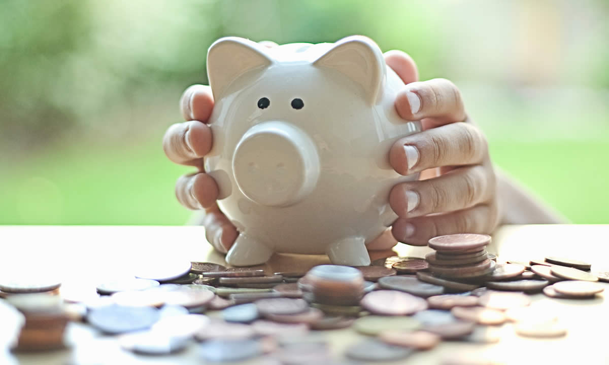 Hands holding a piggy bank and a pile of coins