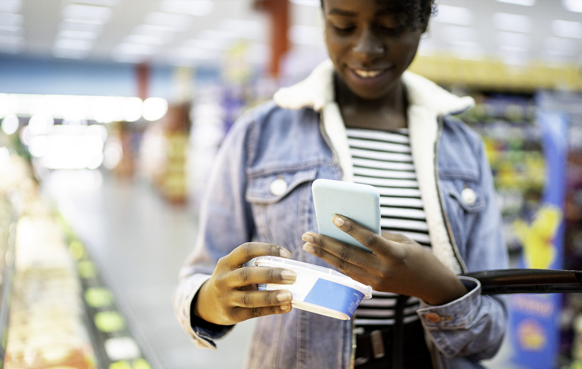 A girl holding up an item in a supermarket and scanning the barcode on her phone