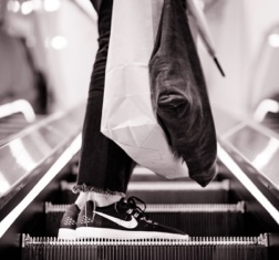 A person wearing trainers and carrying shopping bags standing on an escalator 